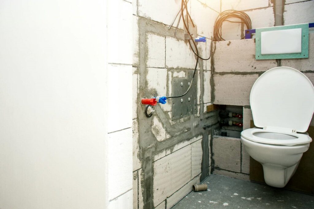 Unfinished bathroom with a wall-mounted toilet and exposed plumbing and wiring.