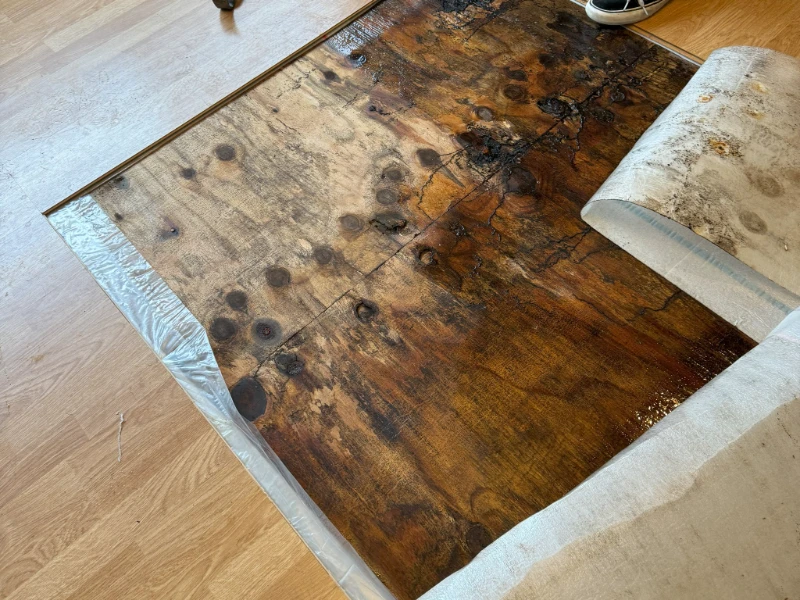Partially peeled back carpet revealing a stained and damaged wooden floor underneath, found during a leak detection service.